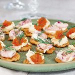 Snittar gjorda av våfflade potatiskroketter med topping av smetana, räkor, rom och dill.