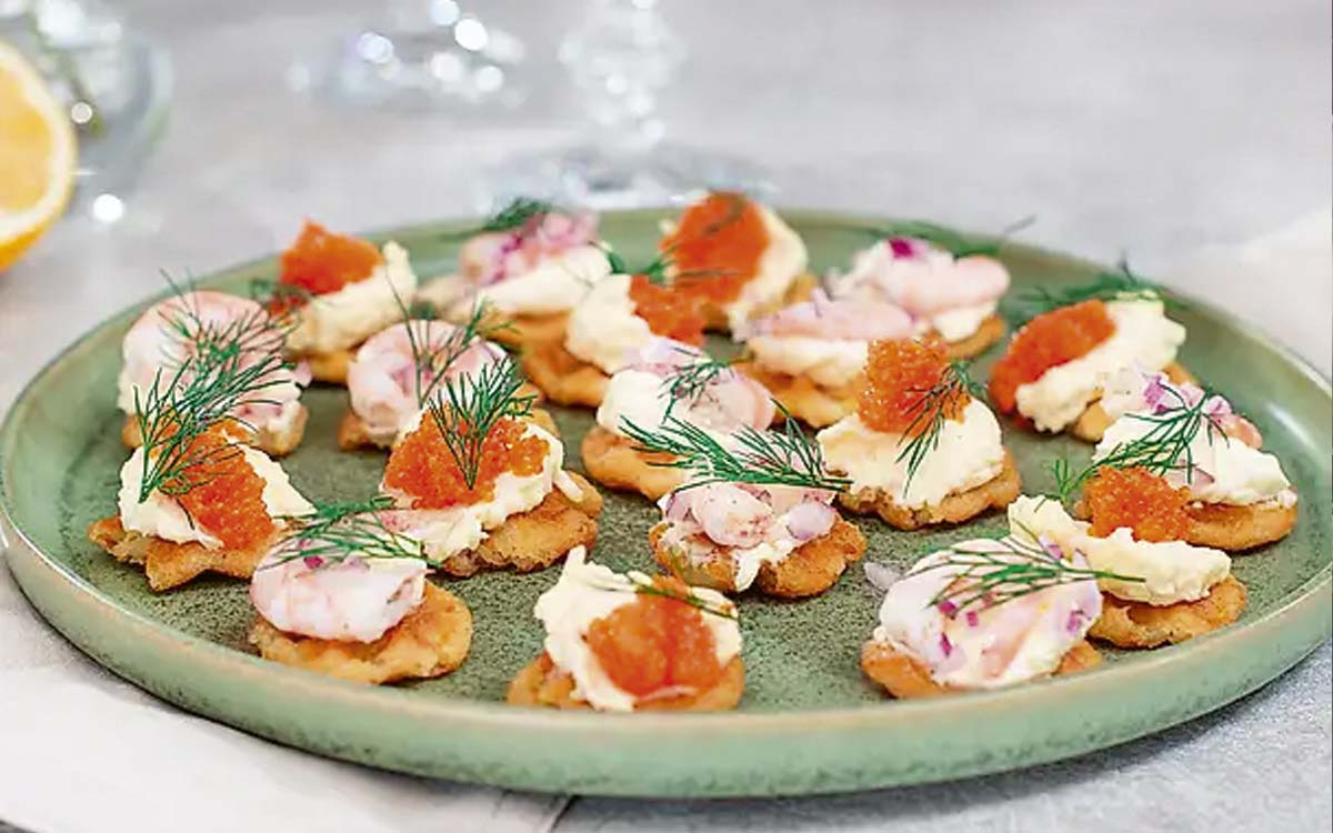 Snittar gjorda av våfflade potatiskroketter med topping av smetana, räkor, rom och dill.