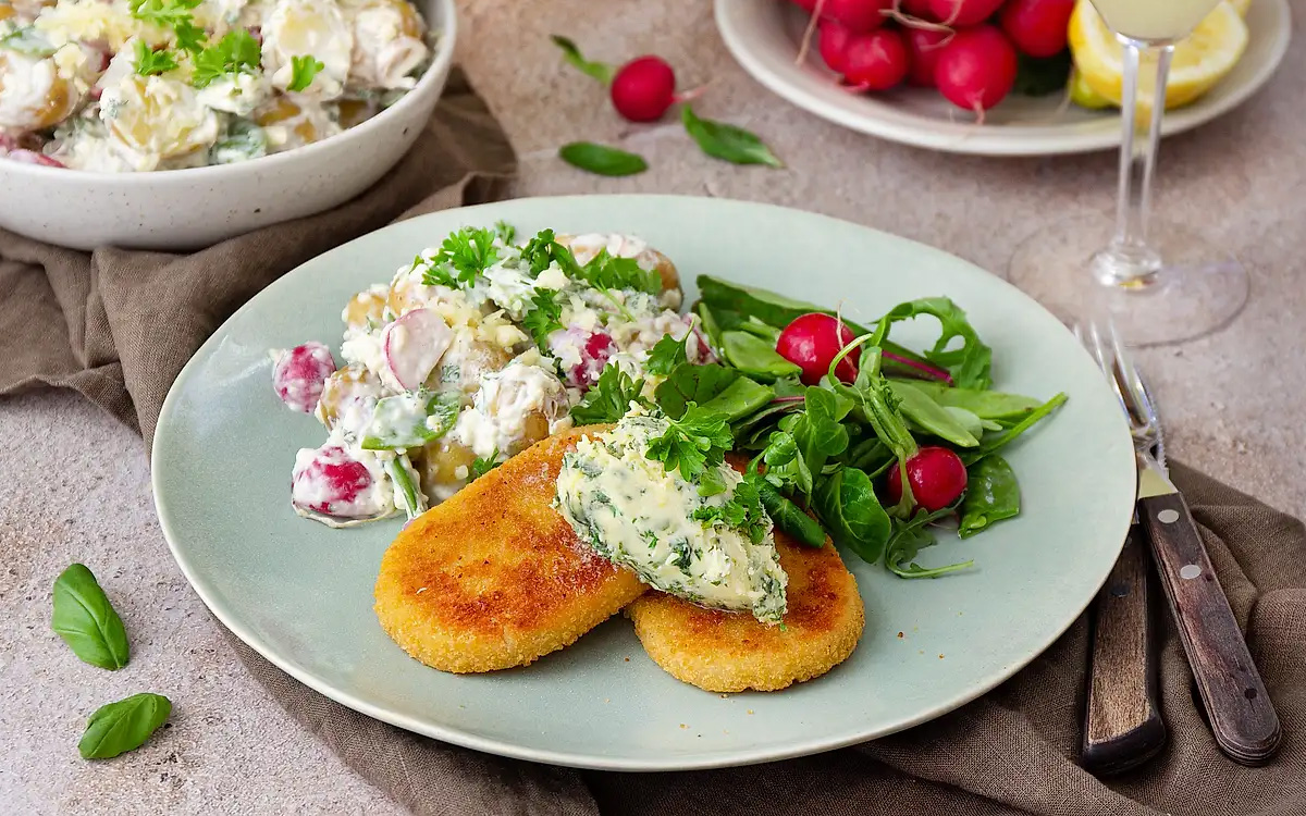 Tallrik med frasig schnitzel, potatissallad, örtsmör, sallad och rädisor.