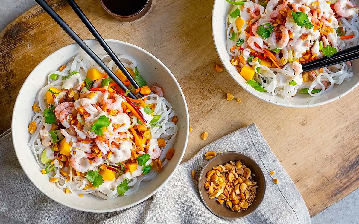 Skålar med asiatisk nudelsallad med räkor, mango, koriander och hackade jordnötter.