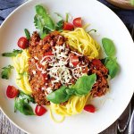 Tallrik med vegetarisk pasta bolognese toppad med parmesan och färska basilikablad.