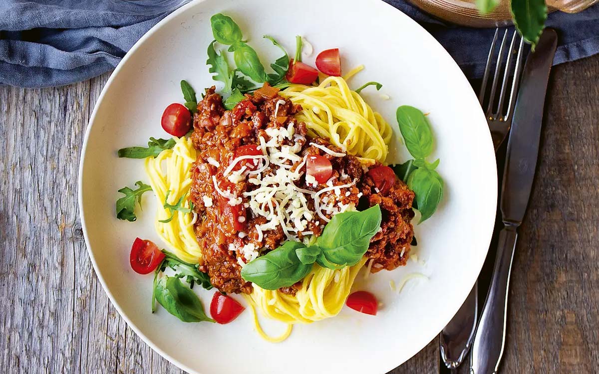 Tallrik med vegetarisk pasta bolognese toppad med parmesan och färska basilikablad.