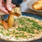 Hand som dippar pommes chips i en skål med fried pickles dip.