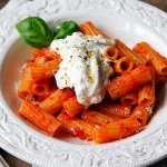 Tallrik med pasta med tomatsås, burrata och basilka.
