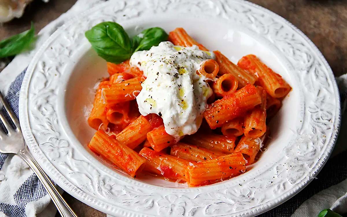Tallrik med pasta med tomatsås, burrata och basilka.