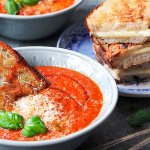 Skål med tomatsoppa toppad med basilika och pamesanost med grilled cheese mackor.