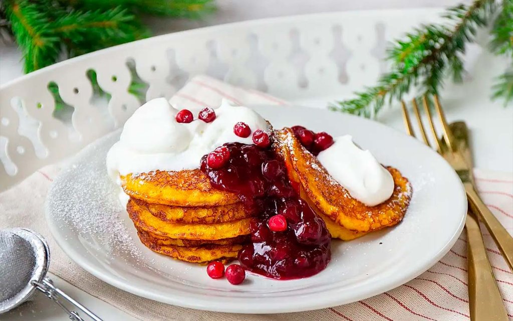 Tallrik med risgrynsgrötplättar med saffran toppade med rårörda lingon och lättvispad grädde.