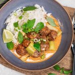 Tallrik med Felix köttbullar i en krämig sås av röd curry toppad med salladslök och thaibasilika serverat med ris.