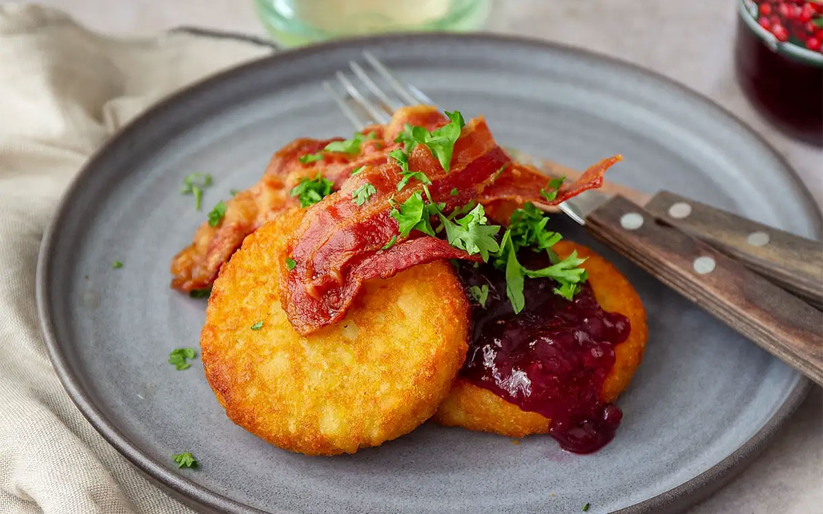 Tallrik med Felix frasiga potatisbullar gjorda i airfryer. Serverade med lingonsylt, knaperstekt bacon och hackad persilja.