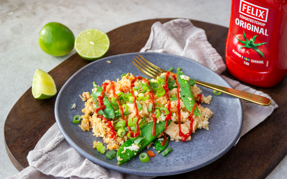 Tallrik med fried rice med sockerärtor, kyckling, ägg och salladslök toppad med Felix tomatketchup.