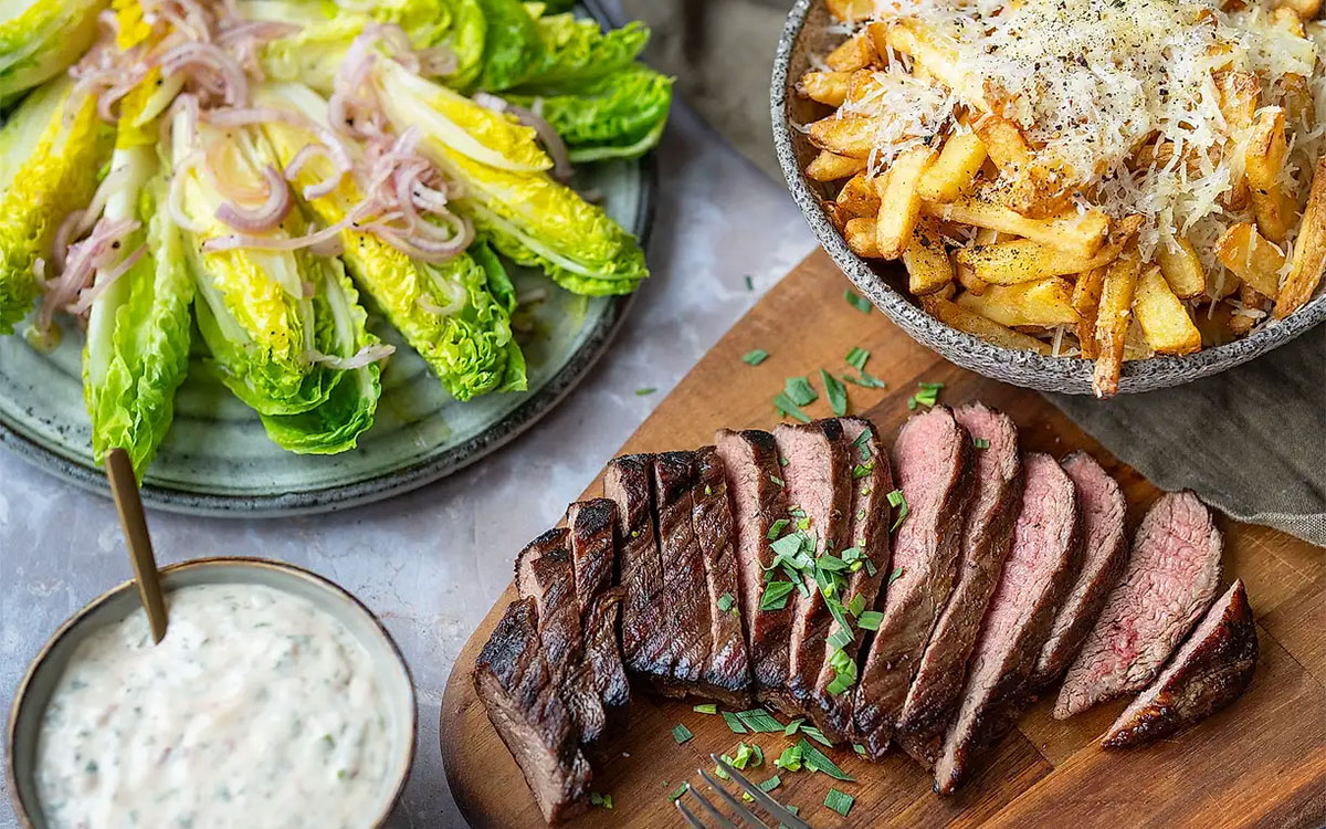 Skivor av grillad flankstek tillsammans med skål med Felix krispiga pommes med parmesan, chilibea och hjärtsallad.
