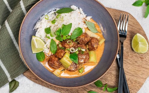 Tallrik med Felix köttbullar i en krämig sås av röd curry toppad med salladslök och thaibasilika serverat med ris.
