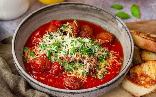 Tallrik med italienska köttbullar i tomatsås toppad med basilika och parmesan.