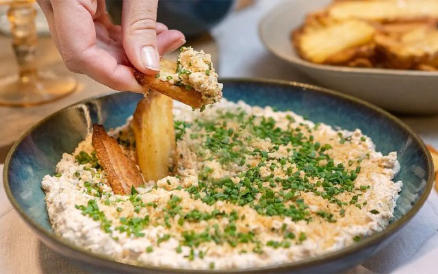 Hand som dippar pommes chips i en skål med fried pickles dip.